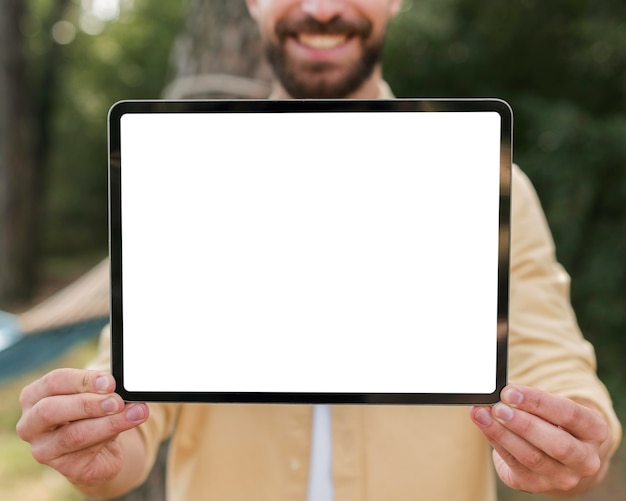 Free photo smiley man holding up tablet while camping outdoors