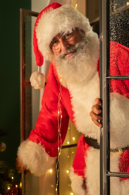 Free photo smiley man in santa costume getting inside house through the window