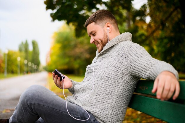 Smiley man with smartphone and earphones on a bench