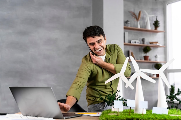 Smiley man working on an eco-friendly wind power project while talking on the phone and using laptop