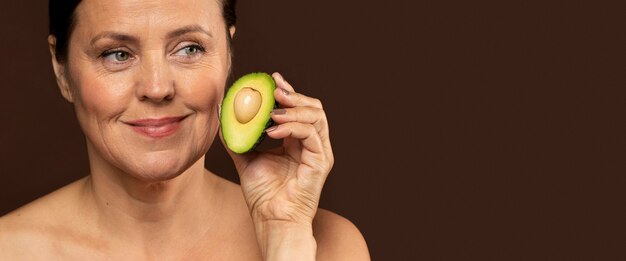 Smiley mature woman holding half of an avocado with copy space