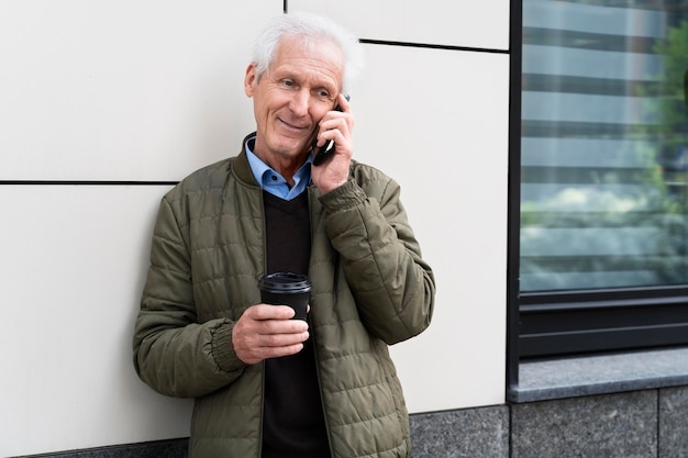 Free Photo smiley older man in the city talking on smartphone while having coffee