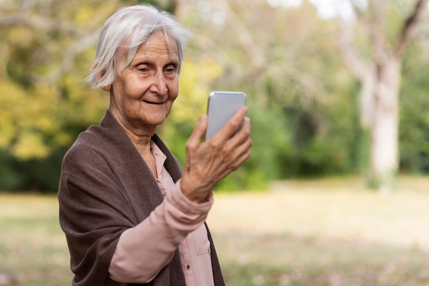 Smiley older woman holding smartphone outdoors