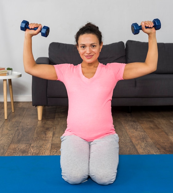 Free photo smiley pregnant woman exercising with weights at home