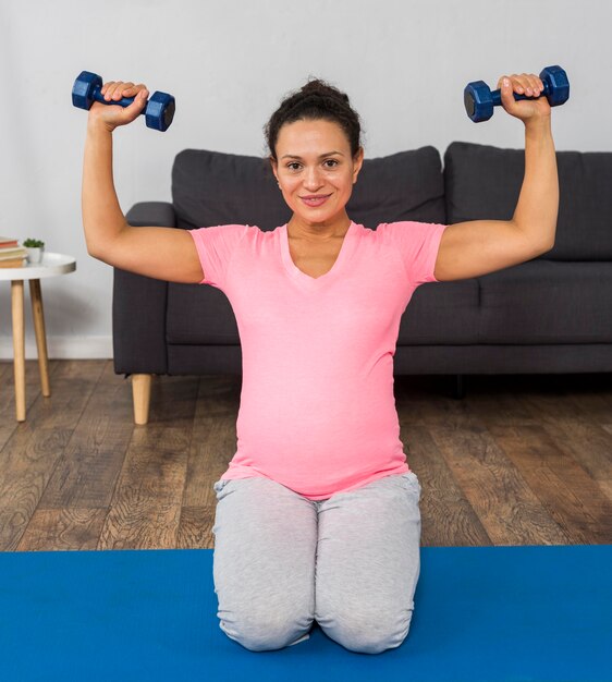 Smiley pregnant woman exercising with weights at home