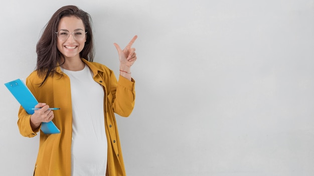 Smiley pregnant woman holding clipboard and pointing up with copy space