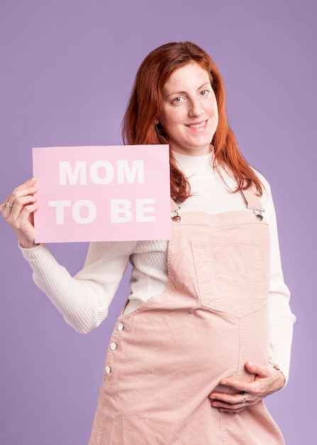 Smiley pregnant woman holding paper with mom to be message