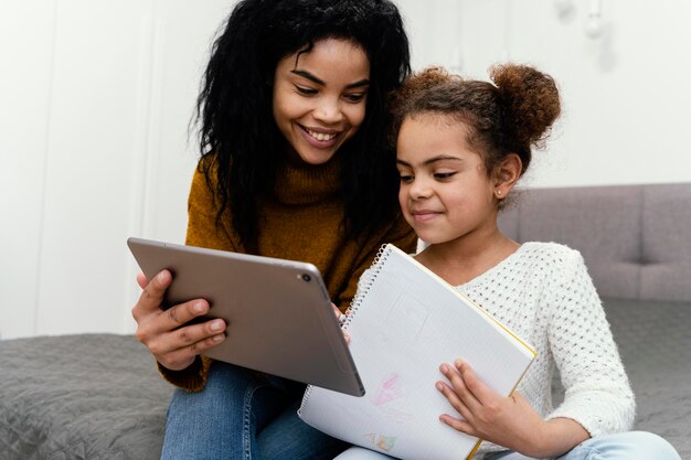 Smiley teenage girl helping sister using tablet for online school