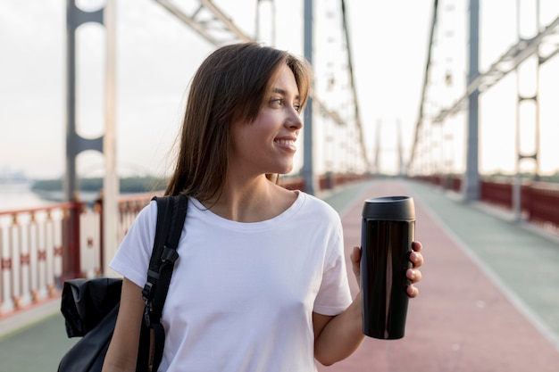 Free Photo smiley traveling woman holding thermos on bridge