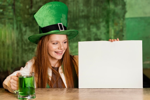 Free photo smiley woman celebrating st. patrick's day at the bar with blank placard and drink