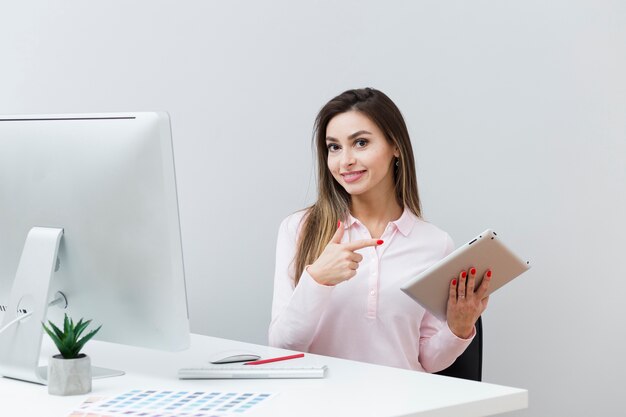 Smiley woman at desk pointing at tablet