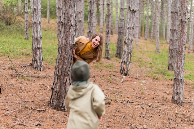 Free photo smiley woman hiding behind a tree from her son