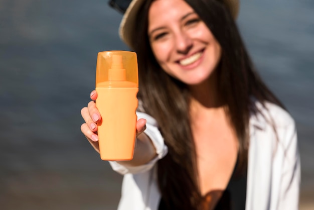 Free photo smiley woman holding bottle of sunscreen at the beach