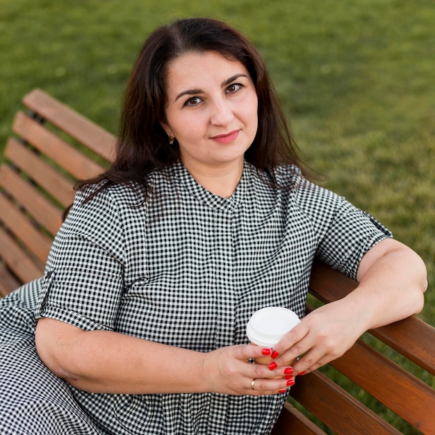 Free photo smiley woman holding a cup of coffee while sitting on a bench