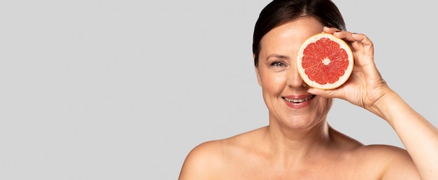 Free photo smiley woman holding half of grapefruit over face with copy space