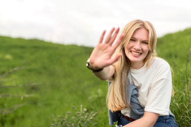 Free Photo smiley woman holding hand up while posing in nature