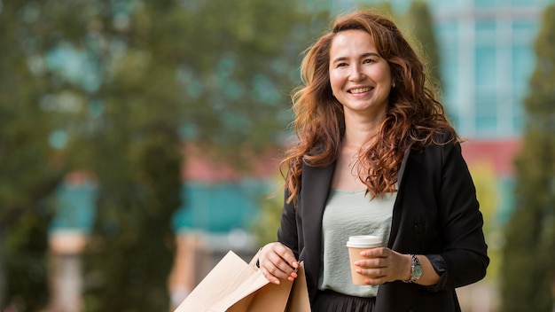 Smiley woman holding shopping bags and a cup of coffee