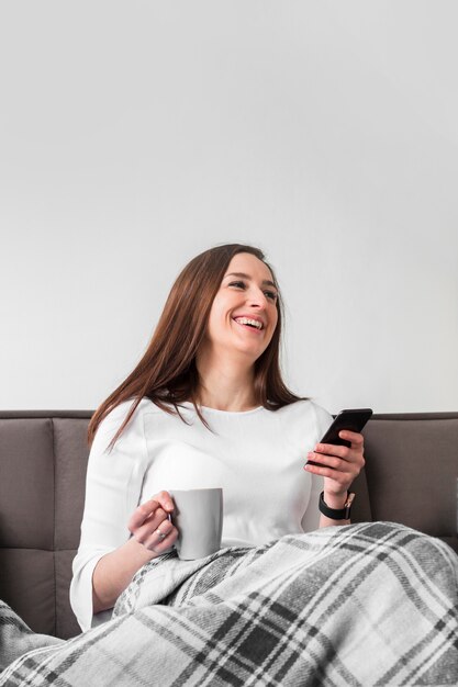 Smiley woman holding smartphone and mug