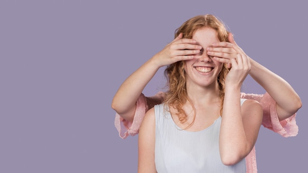 Free photo smiley woman posing with hands covering her eyes with copy space