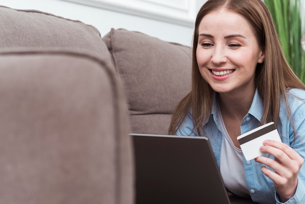 Smiley woman sitting on couch and holding credit card