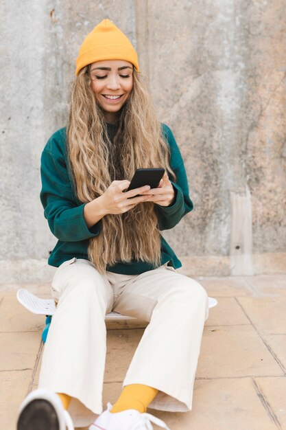 Smiley woman sitting on skateboard while using mobile