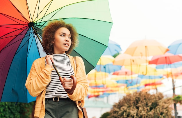 Free photo smiley woman taking a walk outdoors with a rainbow umbrella