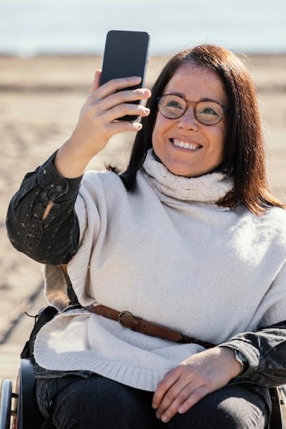 Smiley woman in a wheelchair taking selfie on the beach