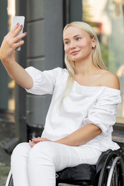 Free photo smiley woman in wheelchair taking selfie with smartphone