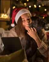 Free photo smiley woman with dog and santa hat holding tablet