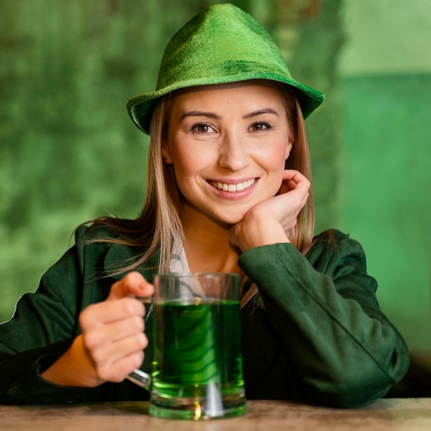 Free Photo smiley woman with hat celebrating st. patrick's day at the bar with drink