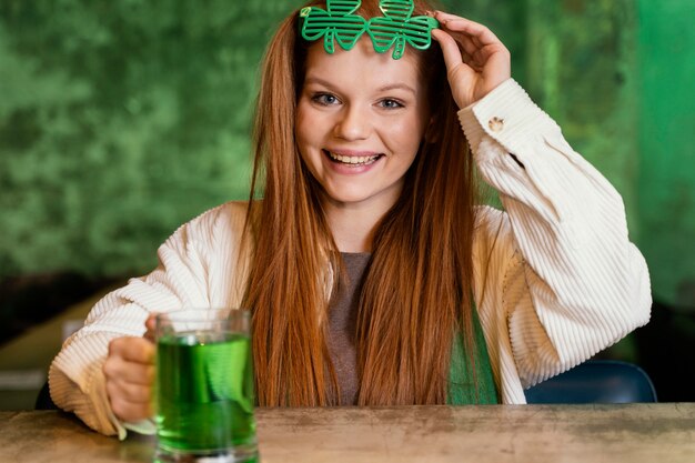 Smiley woman with shamrock glasses celebrating st. patrick's day at the bar