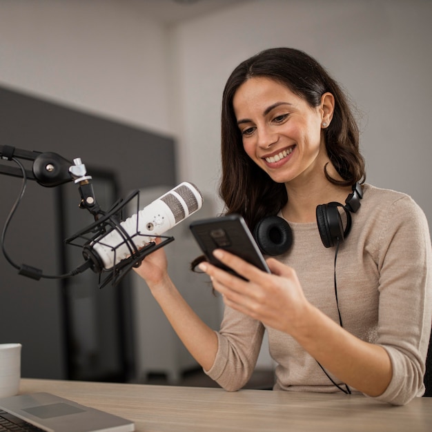 Free Photo smiley woman with smartphone and microphone in a radio studio