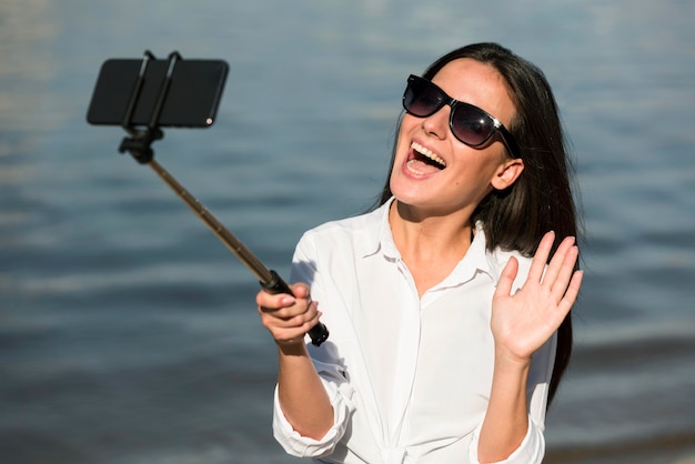 Free photo smiley woman with sunglasses taking selfie at the beach