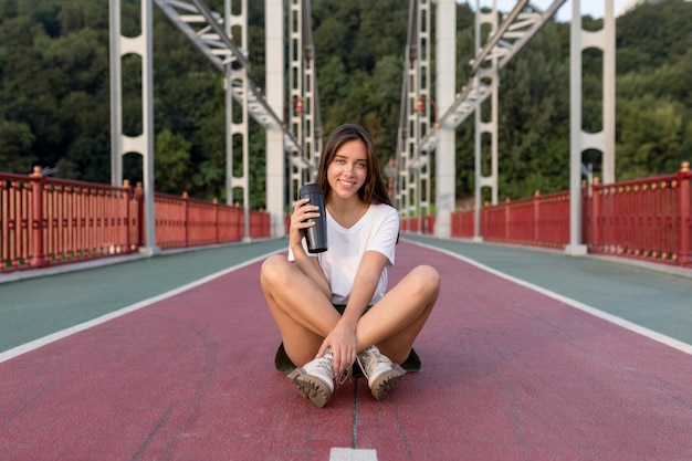 Smiley woman with thermos posing on bridge while traveling