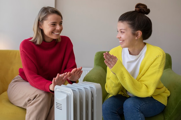 Free photo smiley women getting warm near heater medium shot