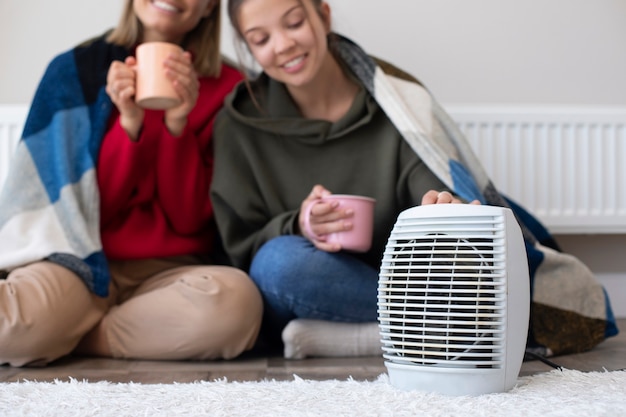 Smiley women with coffee cups near heater