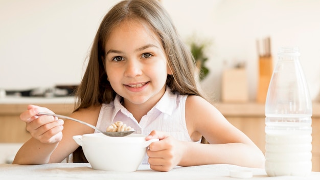 Free photo smiley young girl eating cereals for breakfast