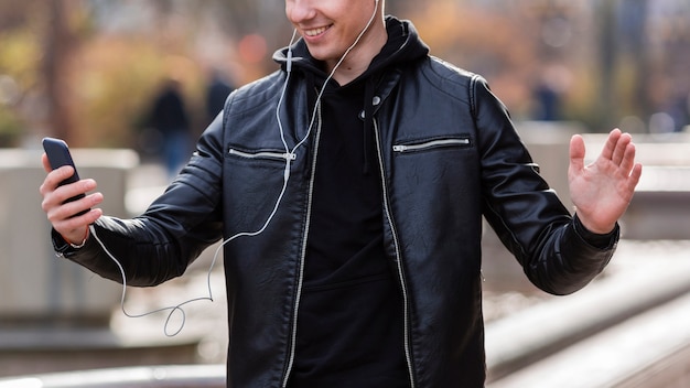 Free photo smiley young man listening to music on earphones outdoors