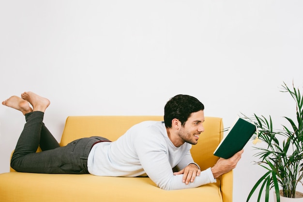 Smiley young man reading a book on the sofa