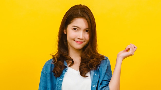 Smiling adorable Asian female with positive expression, smiles broadly, dressed in casual clothing and looking at the camera over yellow wall. Happy adorable glad woman rejoices success.