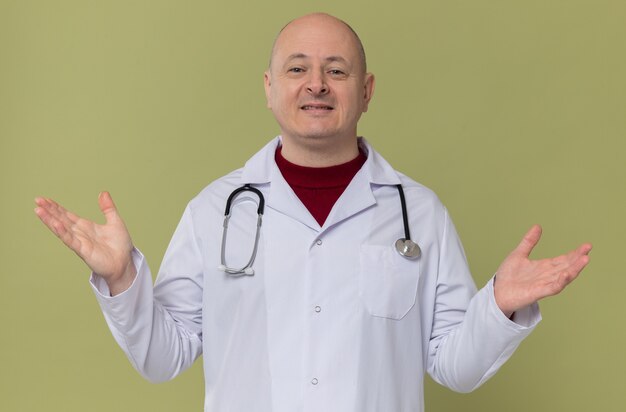 Smiling adult man in doctor uniform with stethoscope keeping hands open 