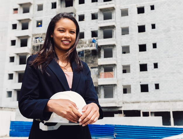 Free Photo smiling african american lady holding safety helmet near building under construction