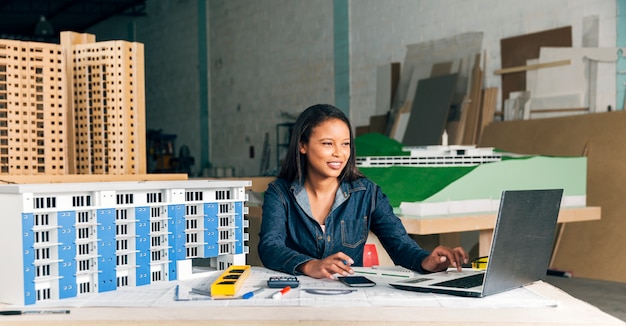 Smiling African-American lady with laptop and model of building