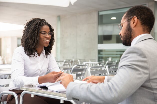 Smiling African American woman in eyeglasses looking at colleague