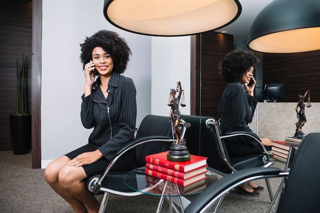 Free Photo smiling african american woman talking on smartphone on armchair in office