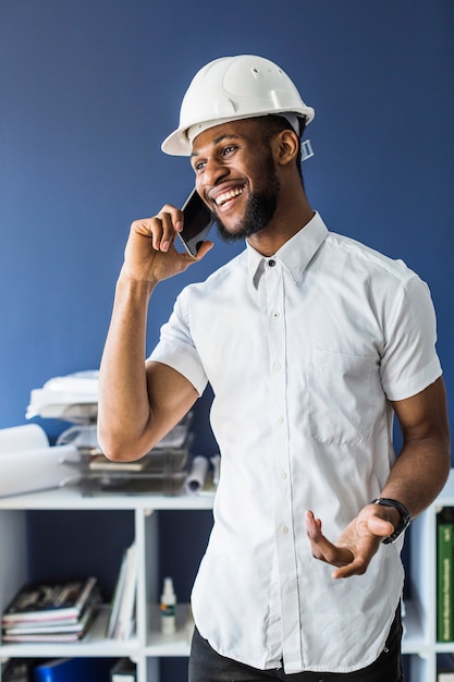 Smiling african architect talking on mobile phone in office