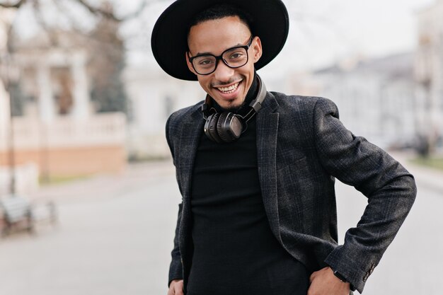 Smiling african man in black sweater posing. Spectacular guy in casual attire enjoying weekend in city.