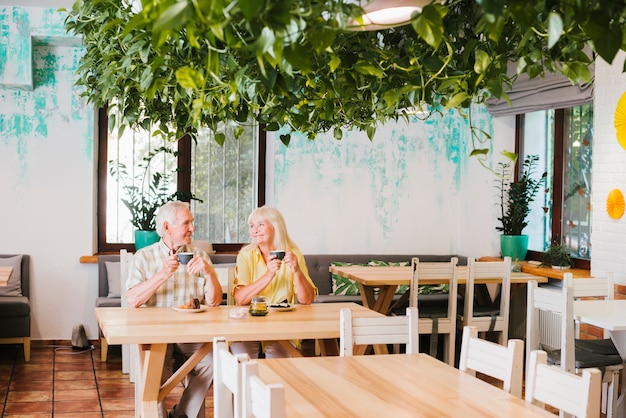 Free photo smiling aged couple sitting in cafe with mugs of tea