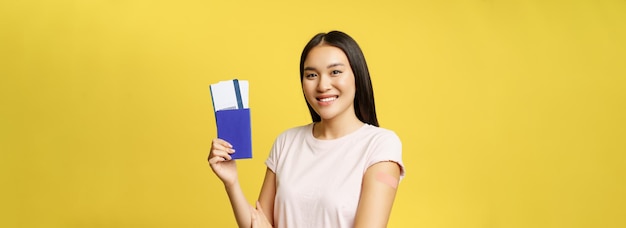 Free photo smiling asian woman showing passport with tickets arm with patch after covid vaccination vaccinating