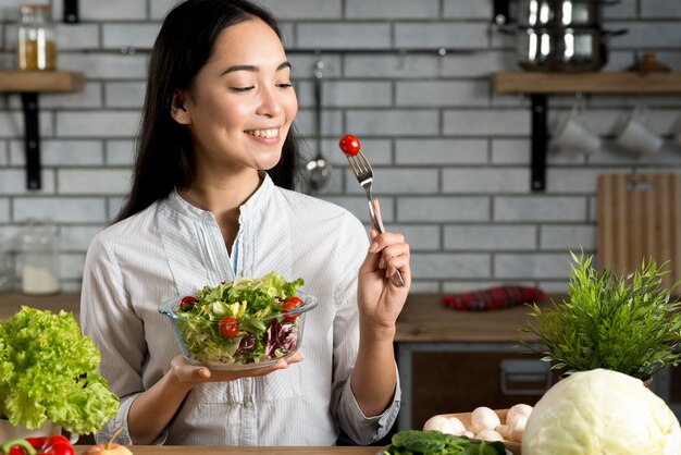 Smiling asian woman with healthy salad in kitchen